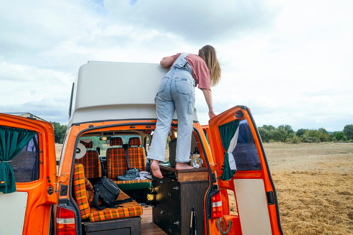 Woman climbing onto a campervan in a rural setting